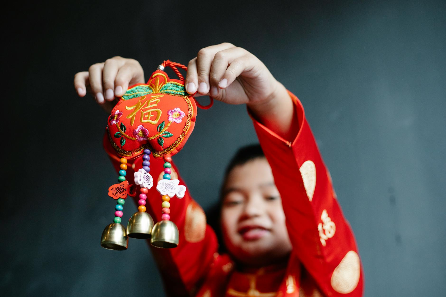Boy in red traditional attire holding a decorated Chinese New Year trinket indoors.