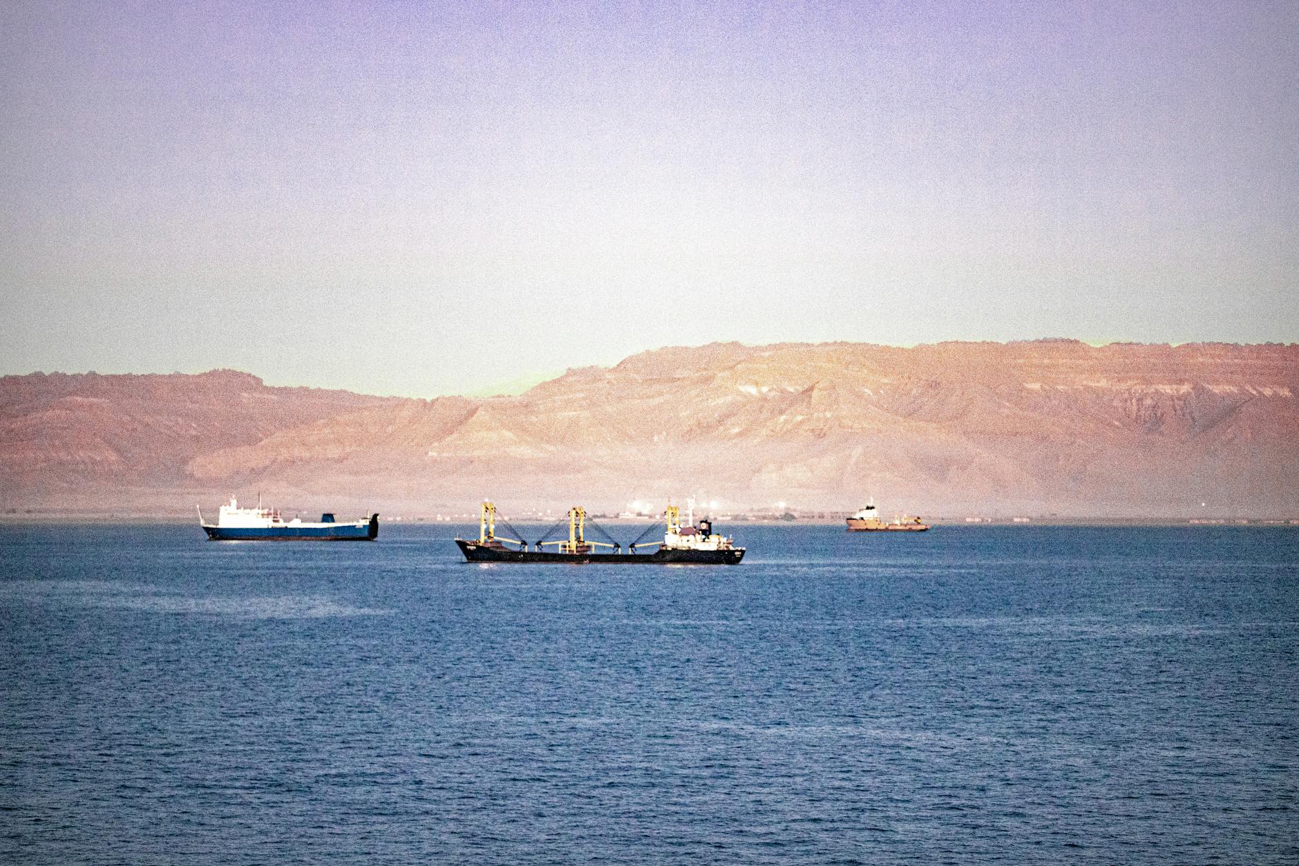 Serene view of cargo ships navigating the Suez Canal with mountains in the background.