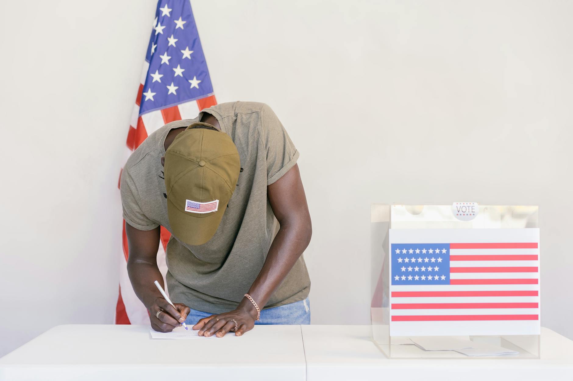Man casting vote at polling station with American flag in background.