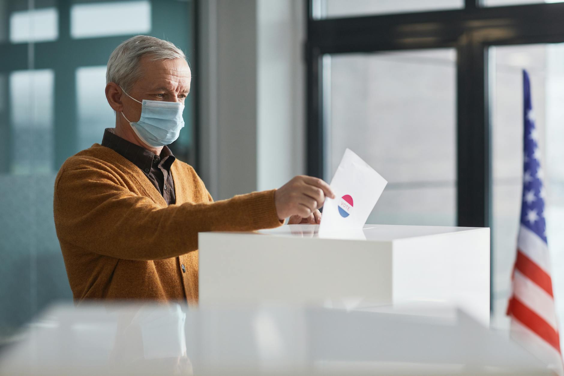 An elderly man wearing a face mask votes in-person, highlighting safety during the pandemic.