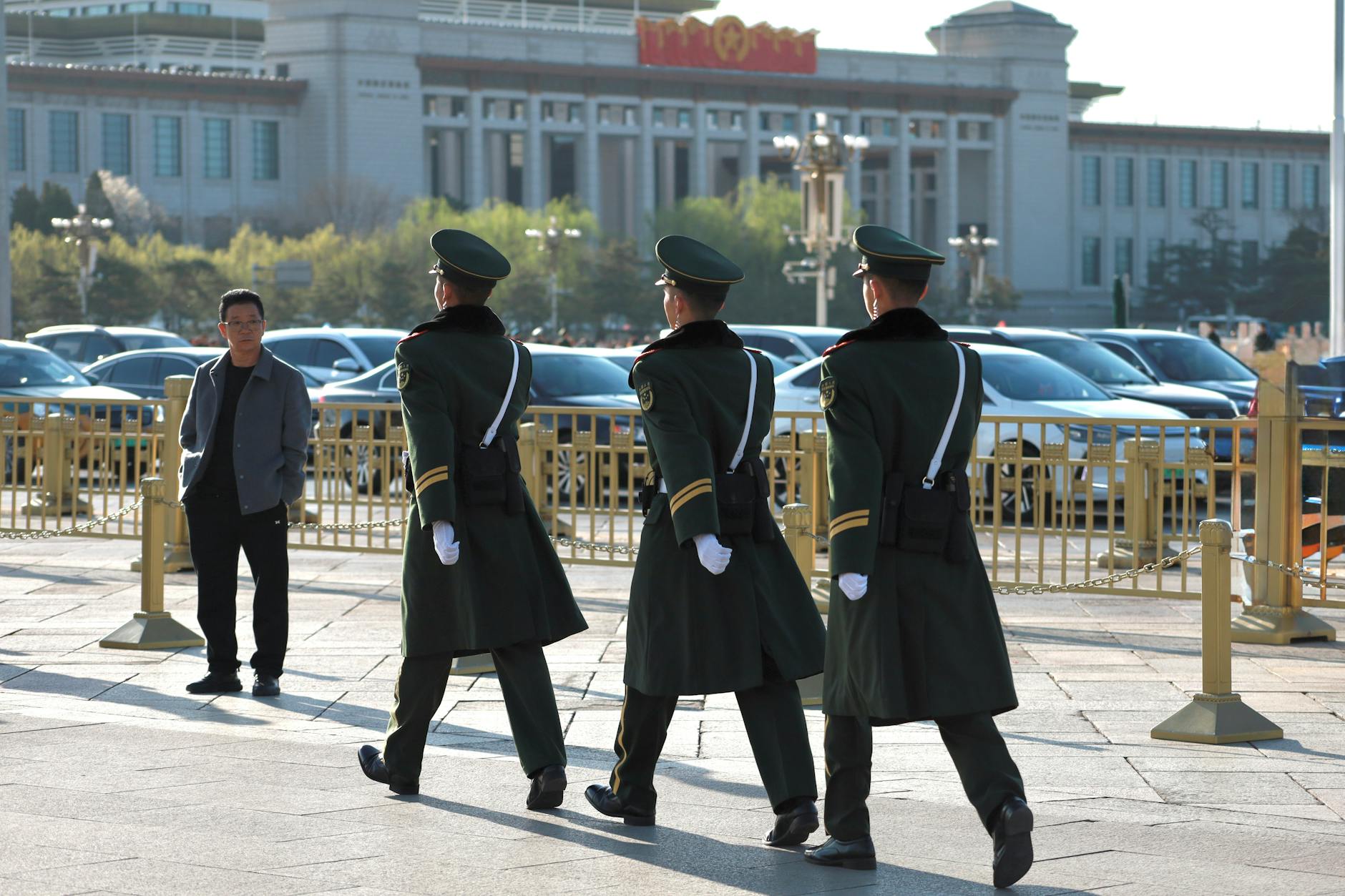 Uniformed guards march in formation outside a grand museum building on a sunny day.