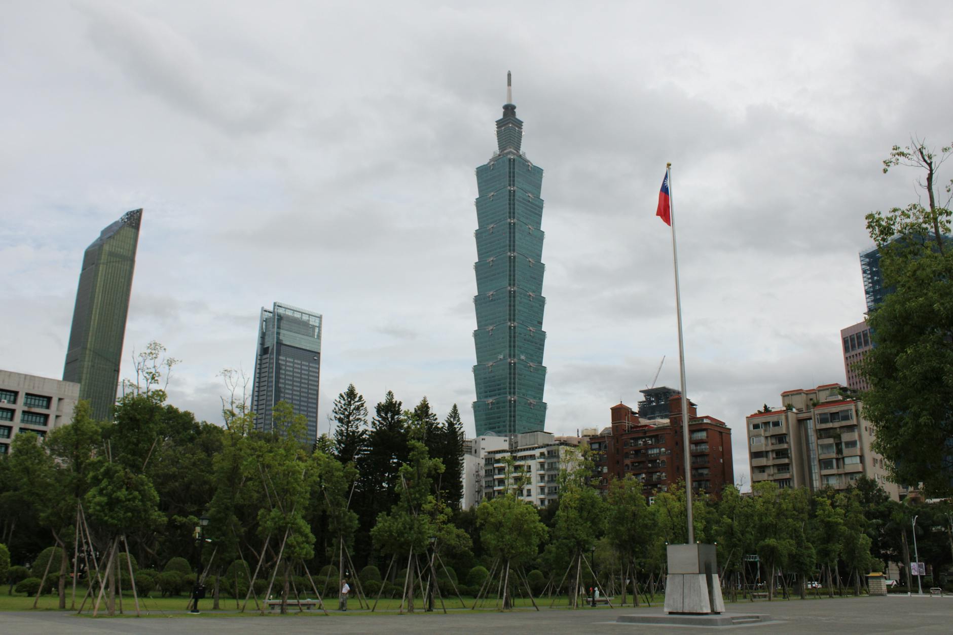 Skyline view of Taipei 101 with cityscape and Taiwanese flag on a cloudy day.