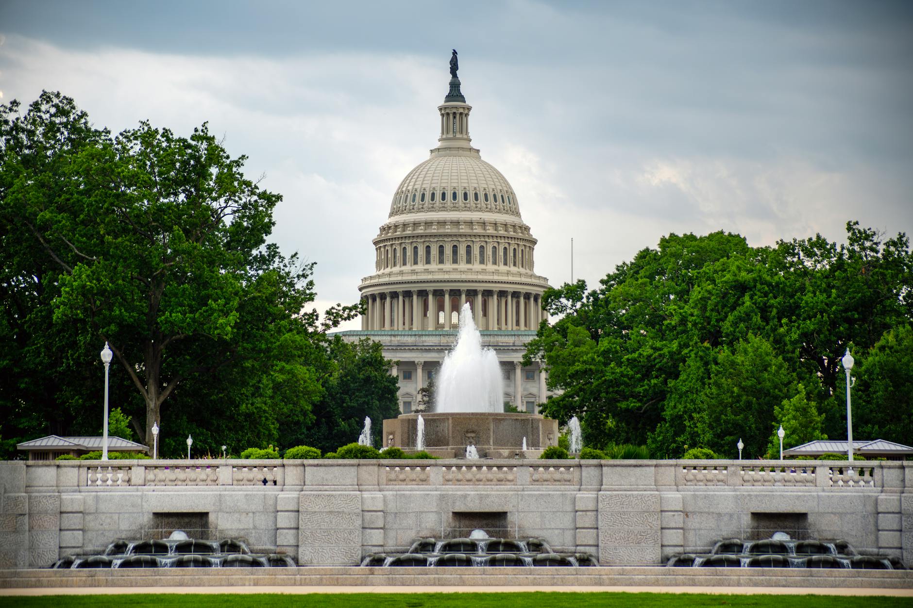 Dramatic view of the US Capitol with a foreground fountain under cloudy skies.