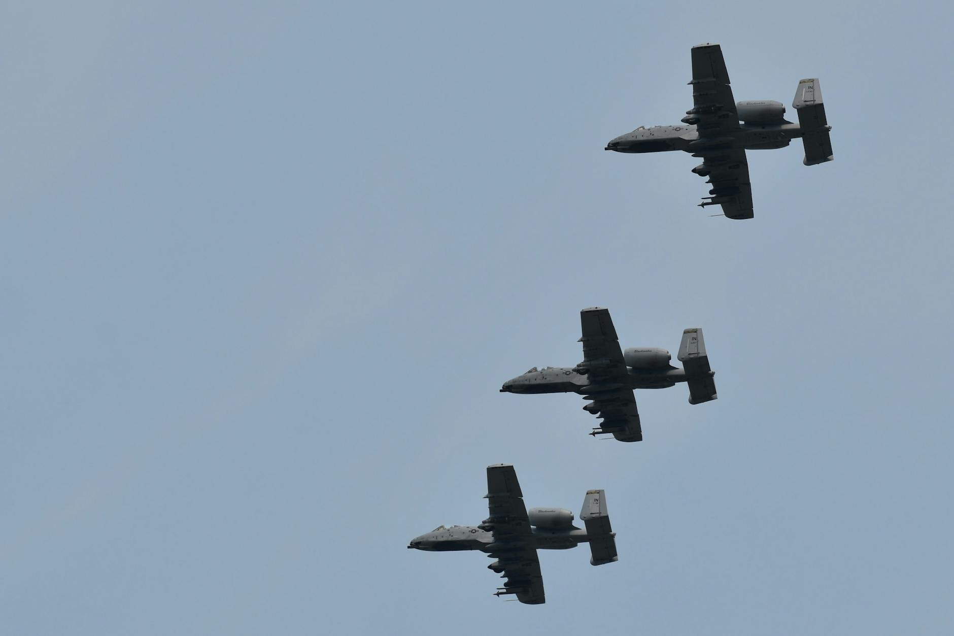 Three A-10 Warthog aircraft flying in formation against a clear blue sky.