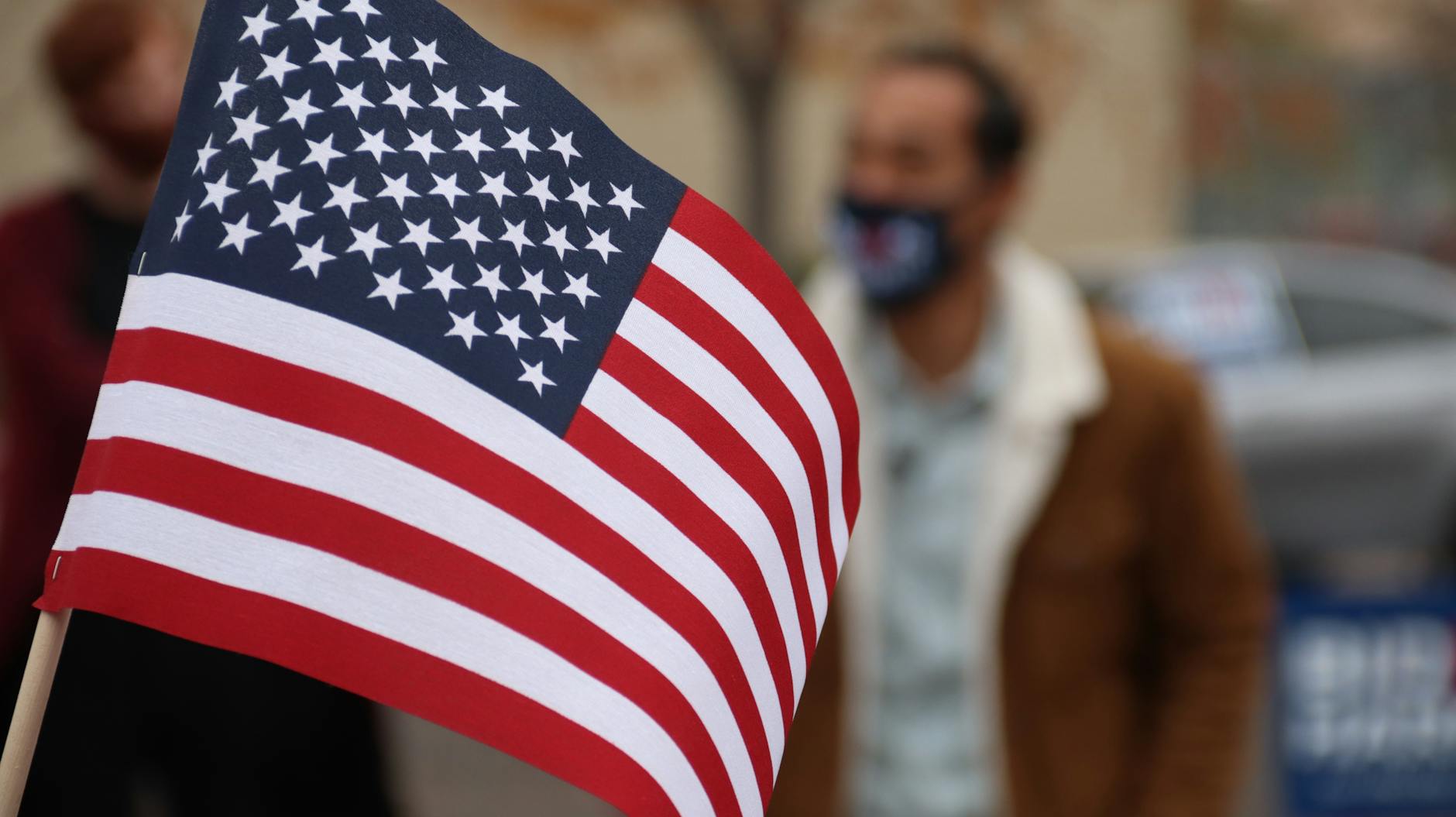 American flag close-up with a person in a mask at an election event.