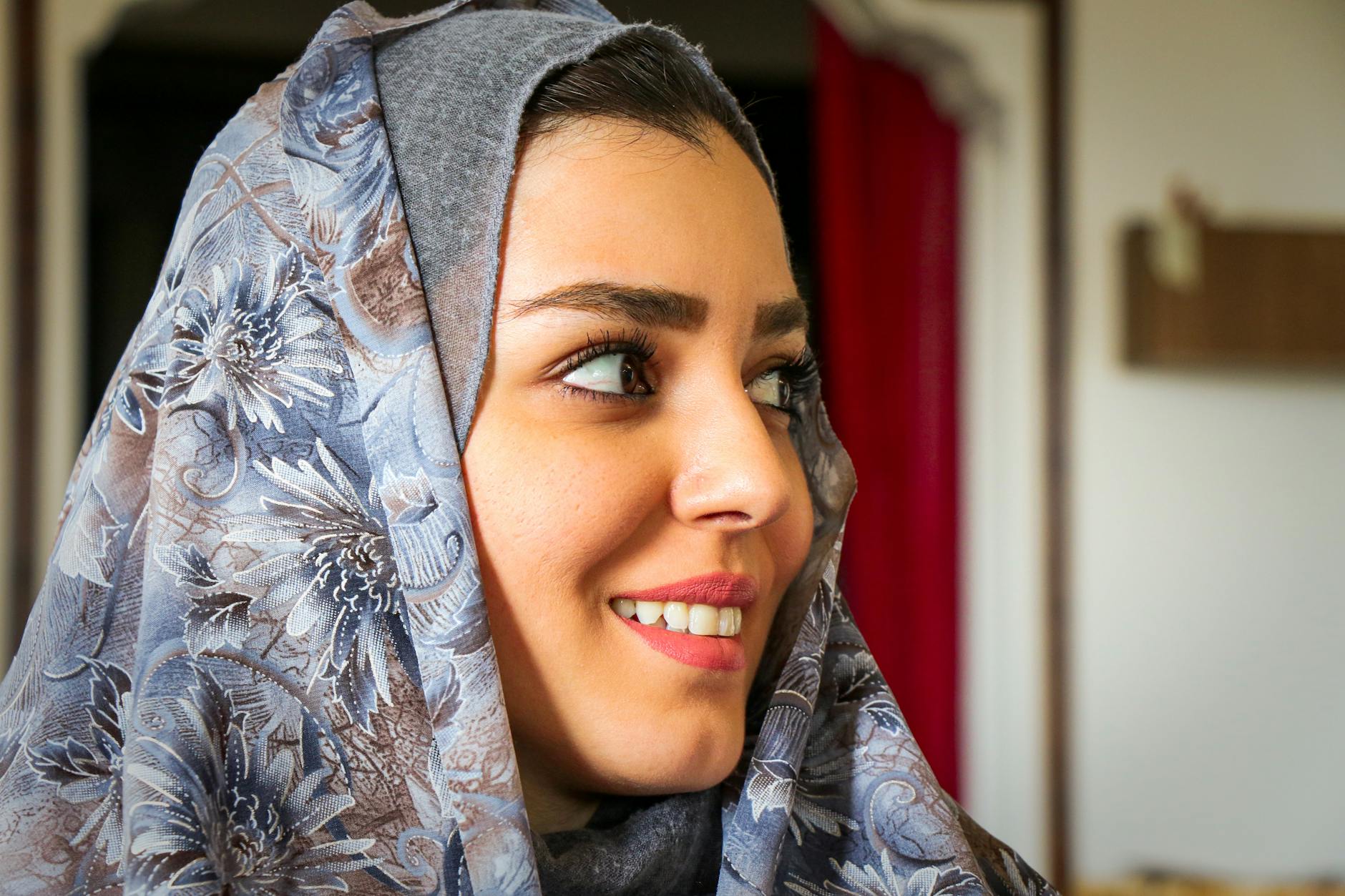 Close-up portrait of a smiling Iranian woman wearing a floral hijab indoors.
