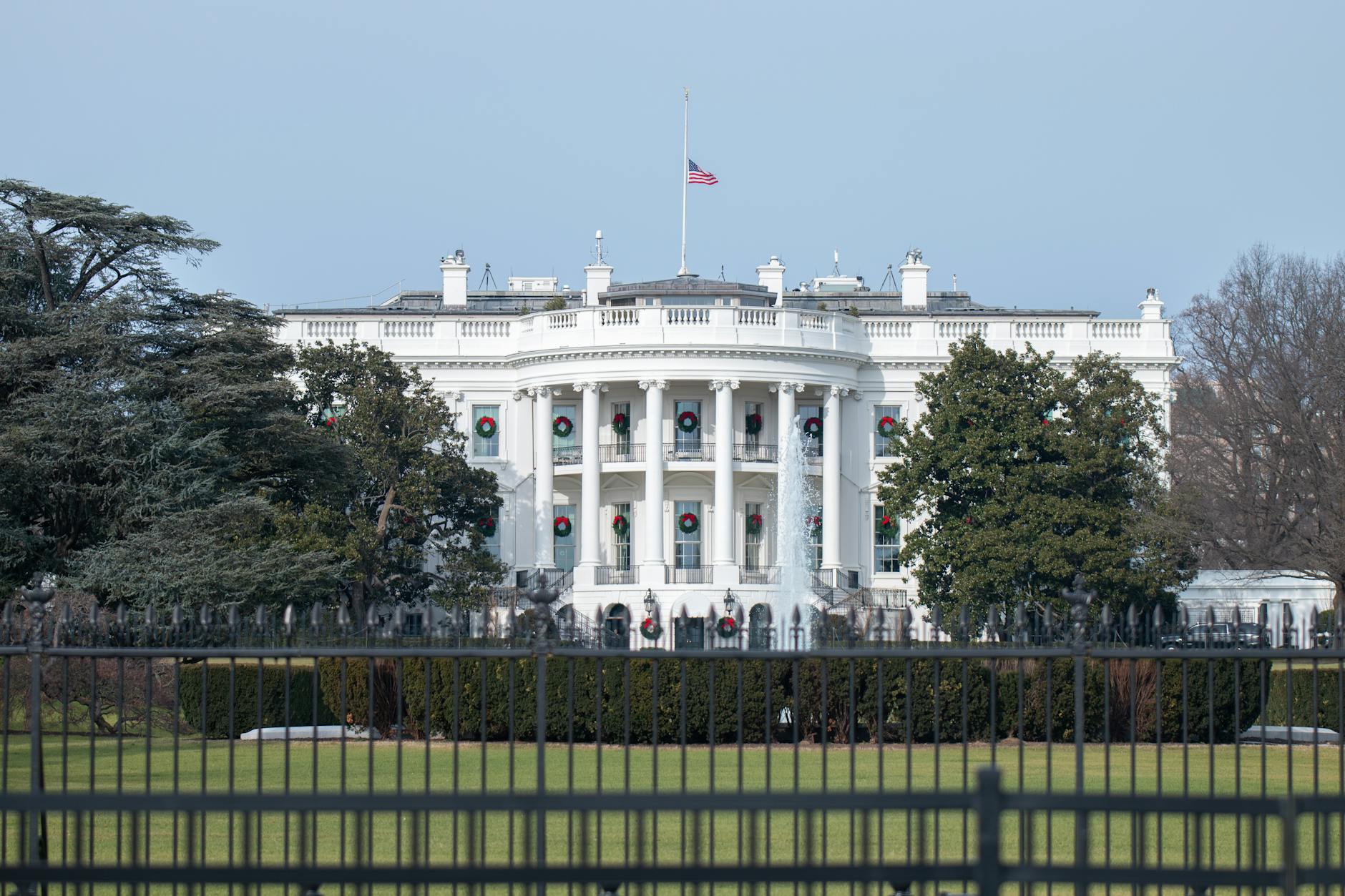View of the White House behind fences in Washington DC, showcasing its iconic architecture and surroundings.