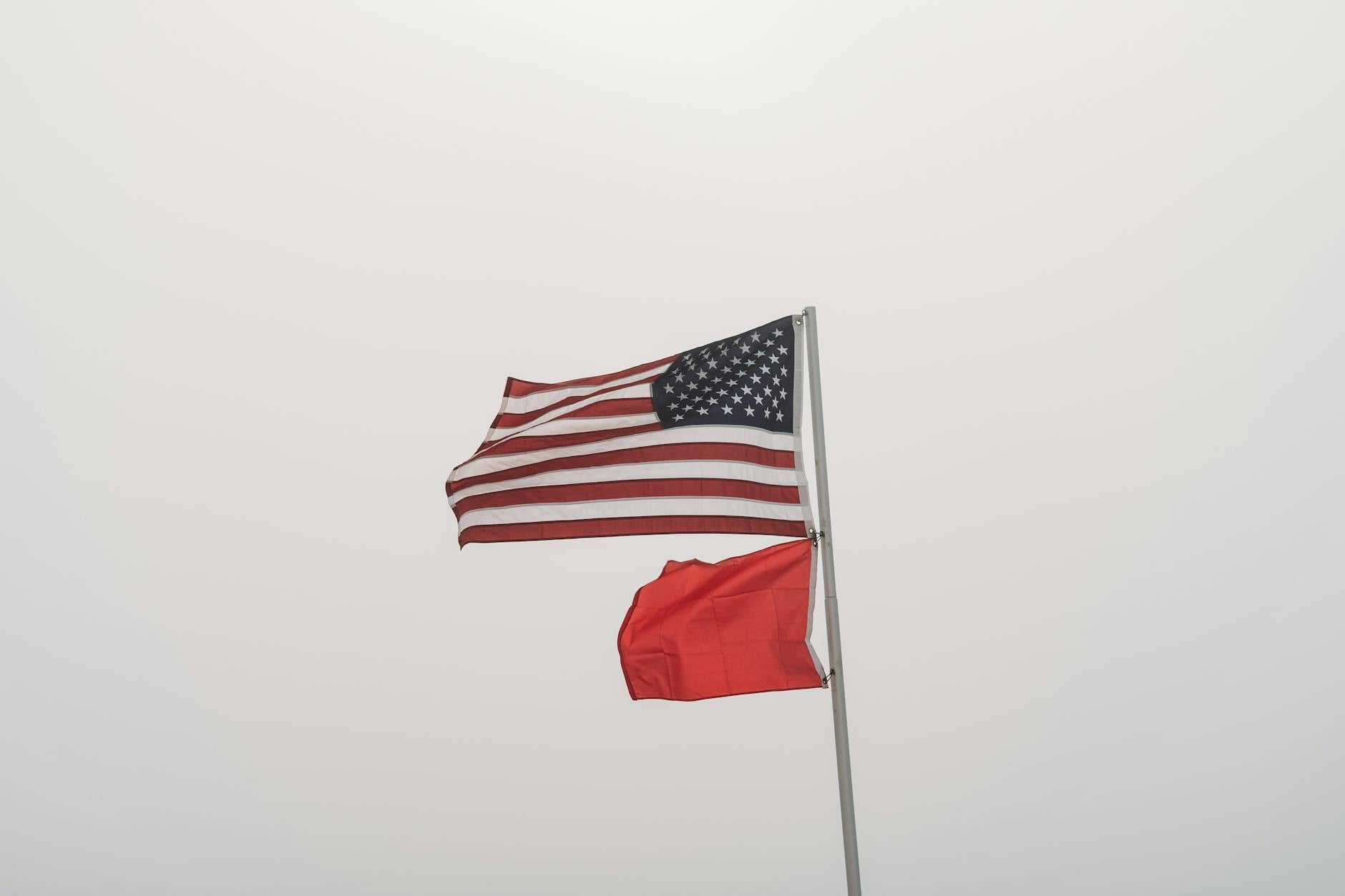 United States and warning flags on display against an overcast sky at Orange Beach, AL.