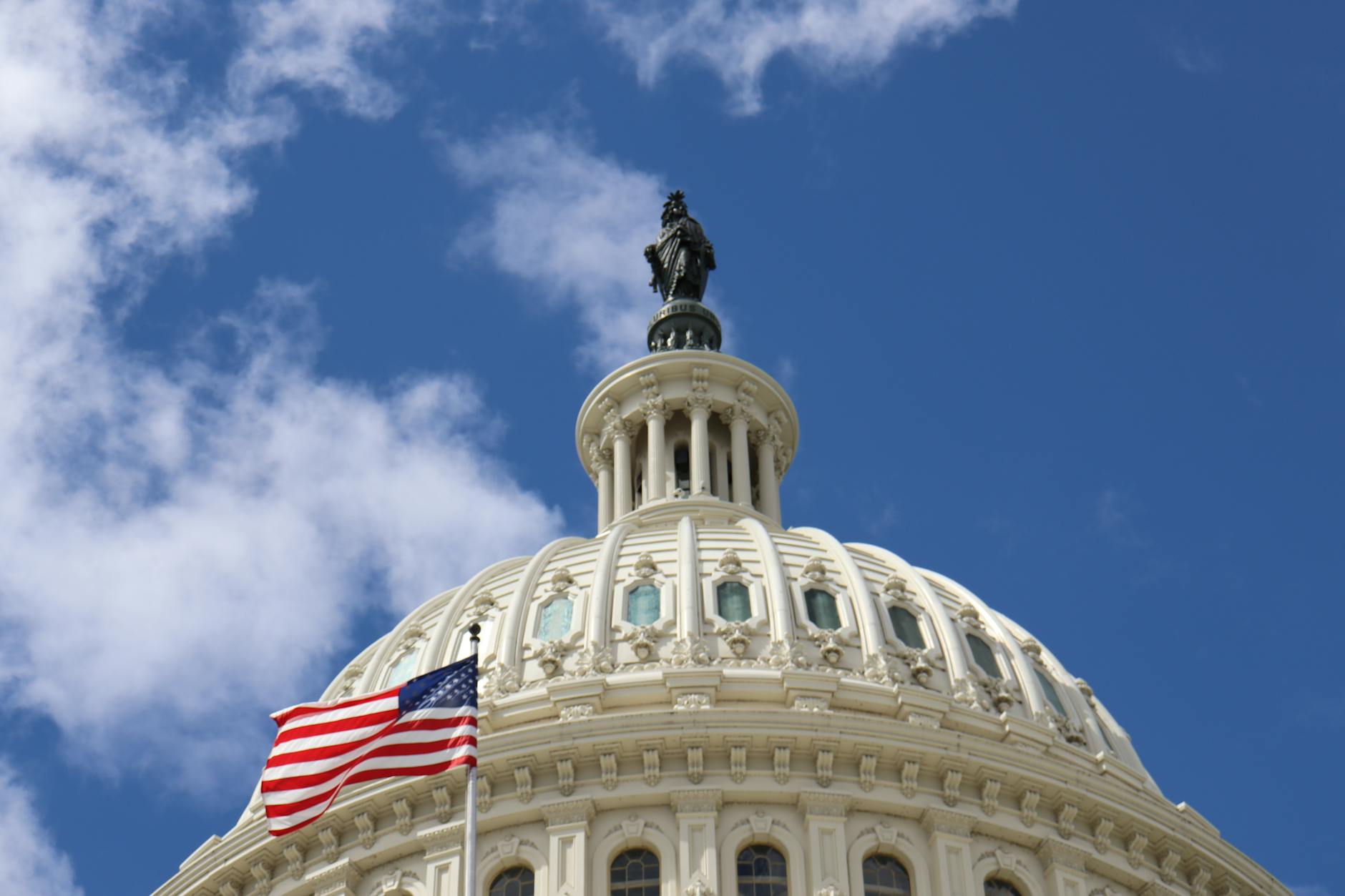 Capture of the U.S. Capitol dome with an American flag waving against a blue sky in Washington, D.C.