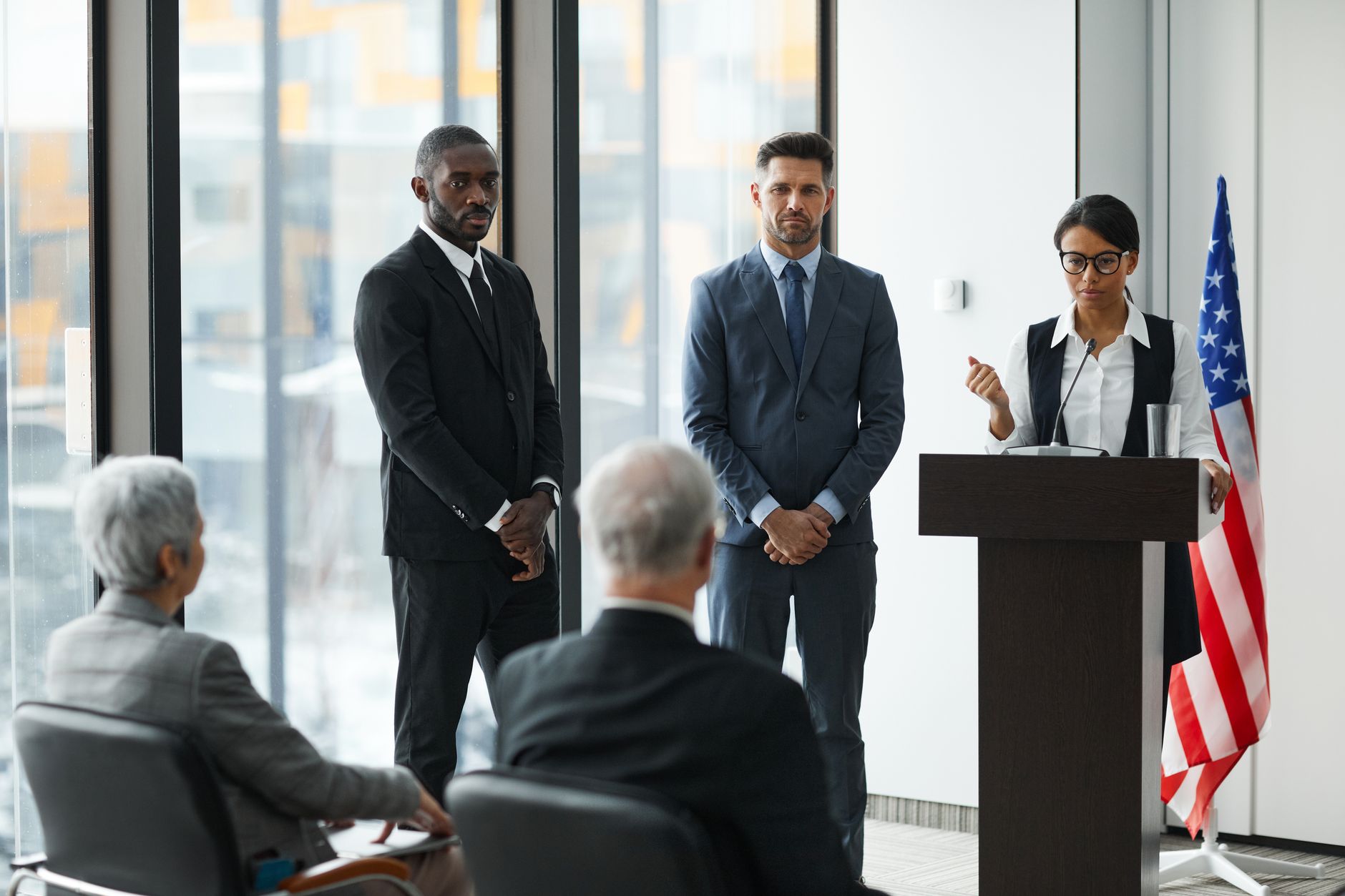 Trump Senate satire image: Professional speakers presenting at a conference in a modern room with glass windows.