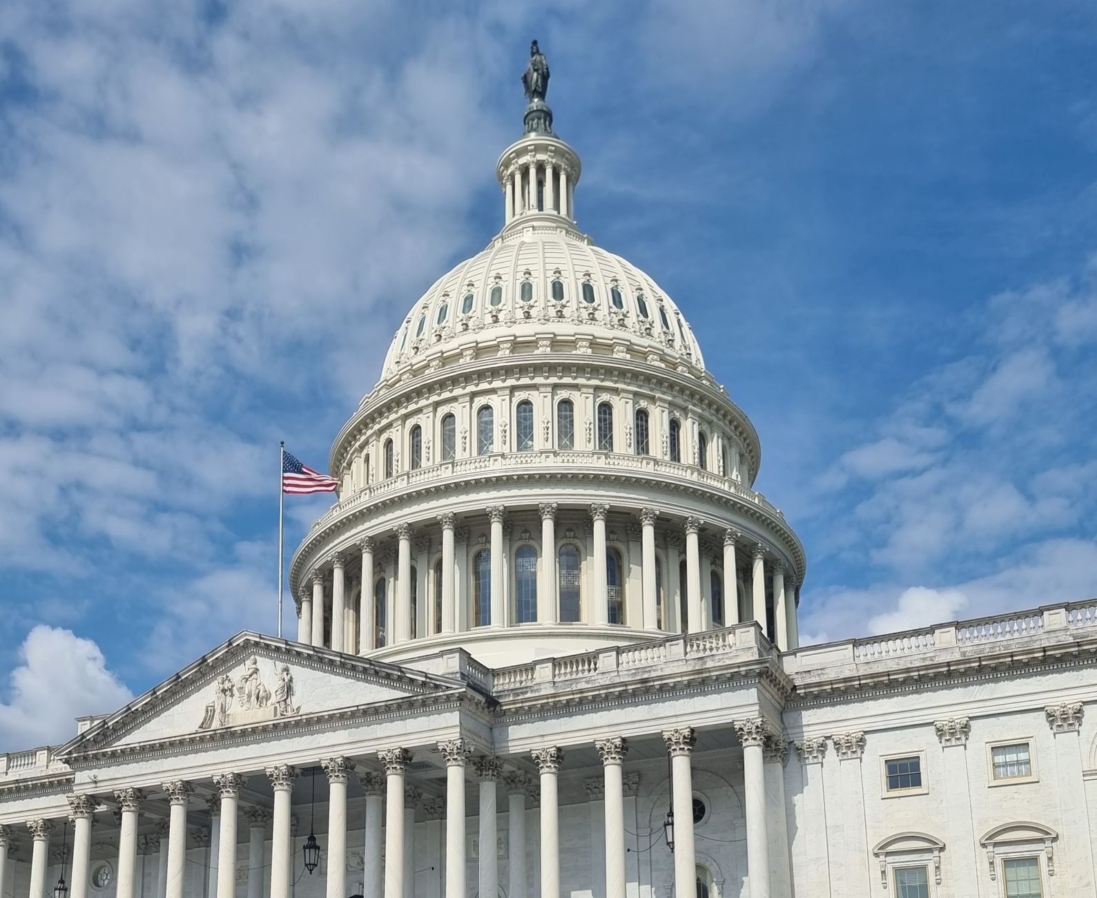 satire-image-25 Trump Republicans satire image: A striking view of the US Capitol dome with flag and blue sky in Washington, DC.