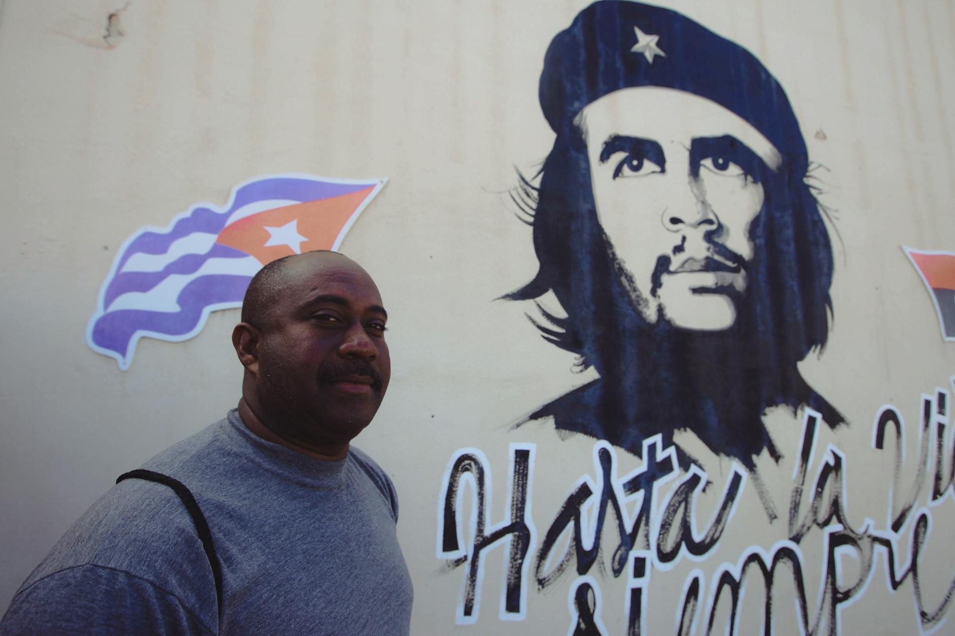 satire-image-26 White House Classifies satire image: African American man with Che Guevara mural and Cuban flag in the background, outdoor setting.
