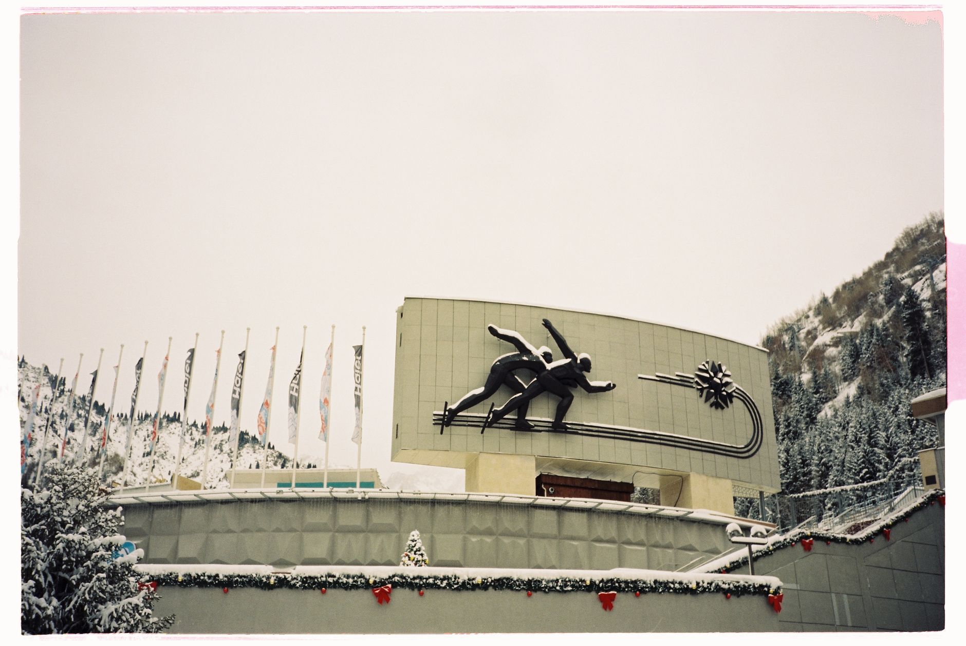 satire-image-42 Election Ski satire image: Sculpture of ice skaters at snowy winter sports venue, flags in background.