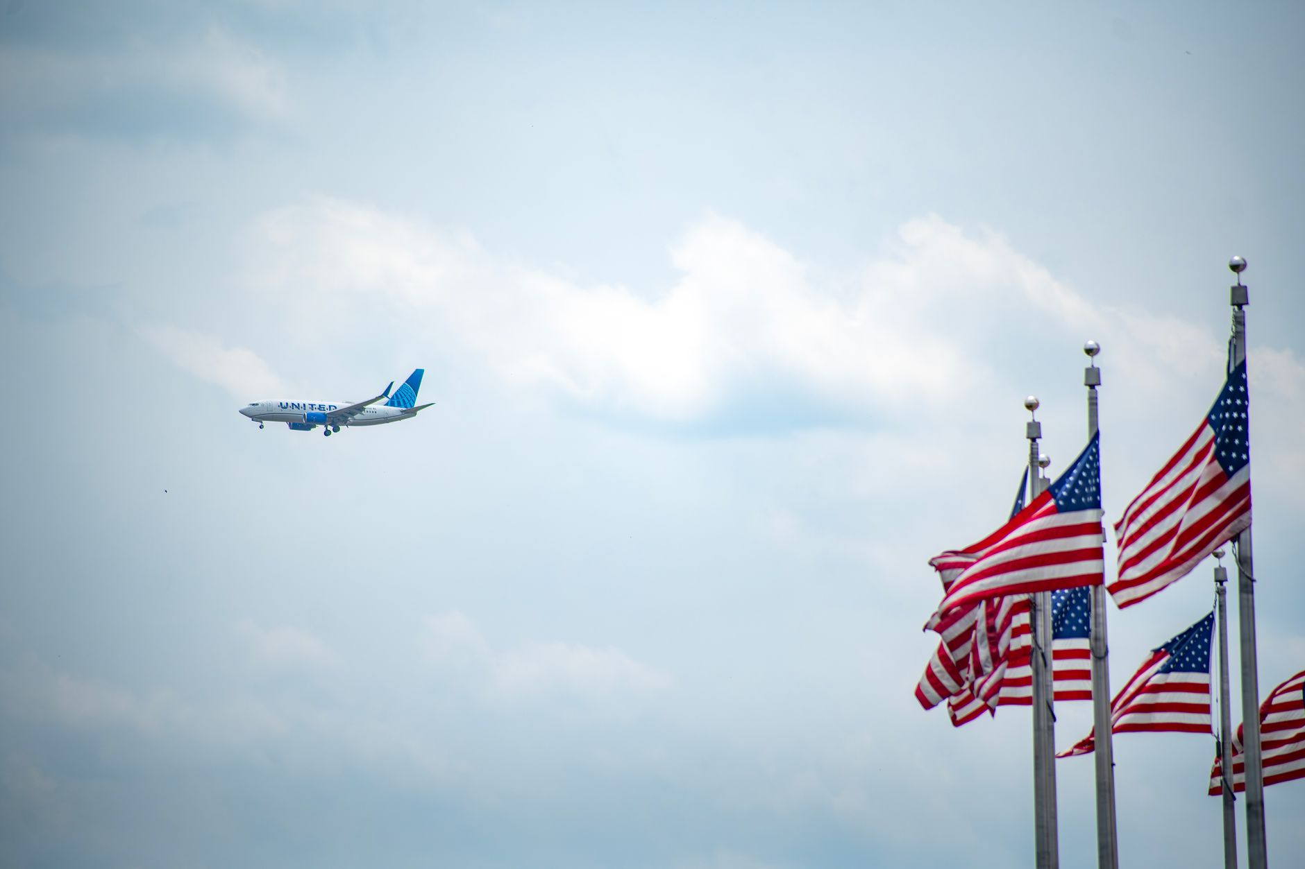 Trump Prepares satire image: Airplane flying near waving American flags against a bright blue sky, symbolizing travel and patriotism.