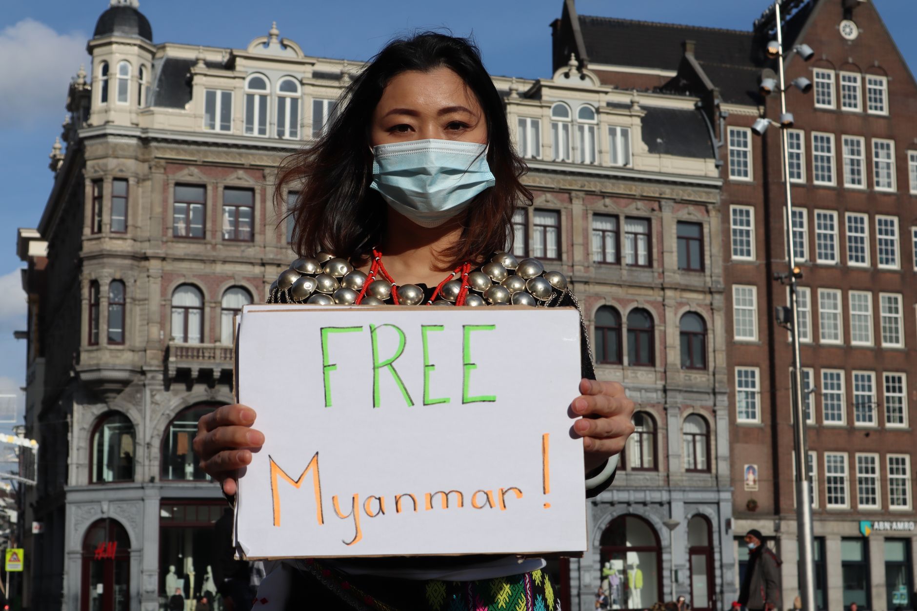 satire-image-51 China Arrest satire image: Woman protesting with a sign for Myanmar freedom in urban backdrop, wearing a mask.