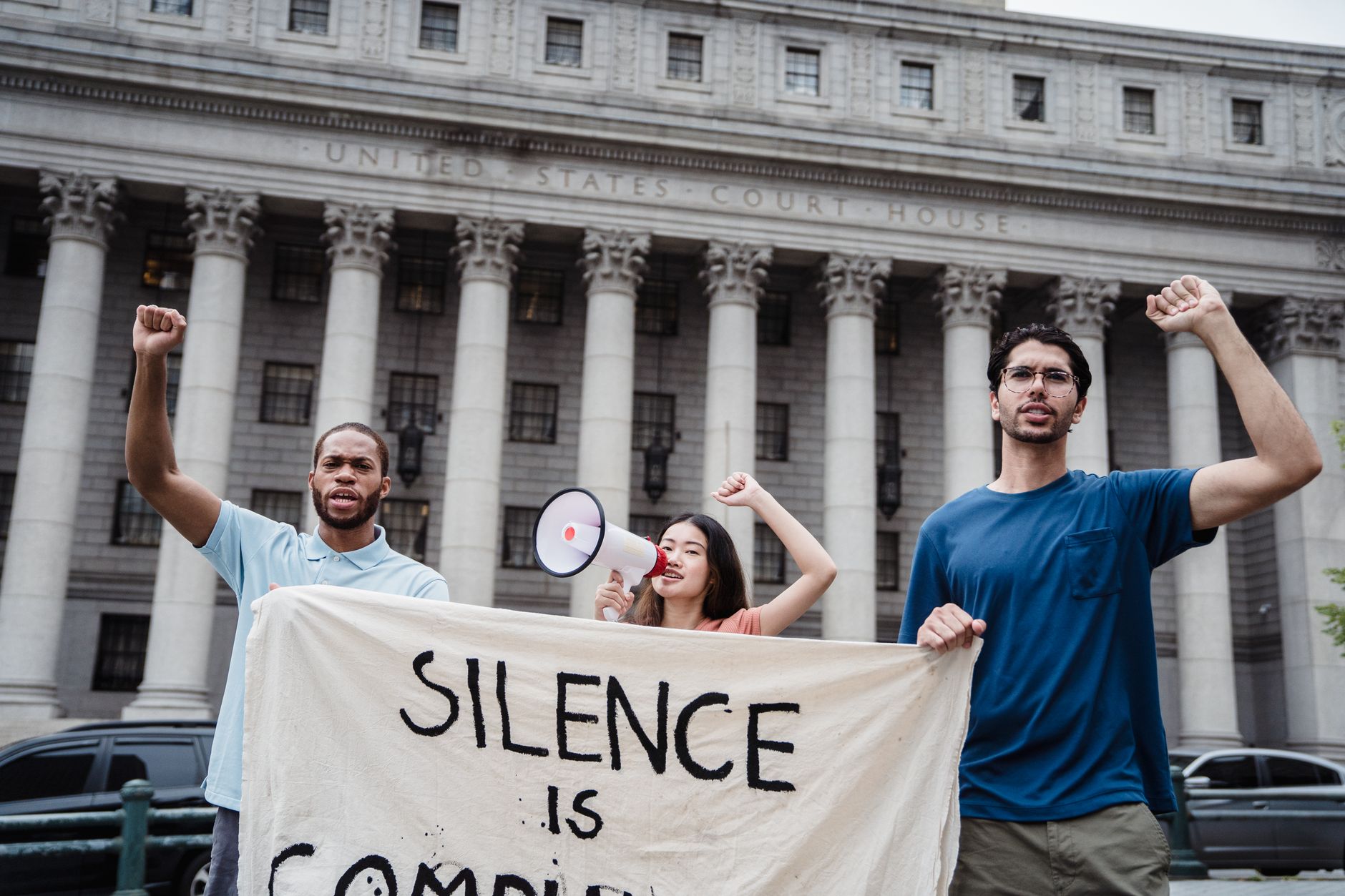 satire-image-55 Supreme Court Treats satire image: Group of diverse activists holding banner and megaphone in front of a US courthouse for a protest.