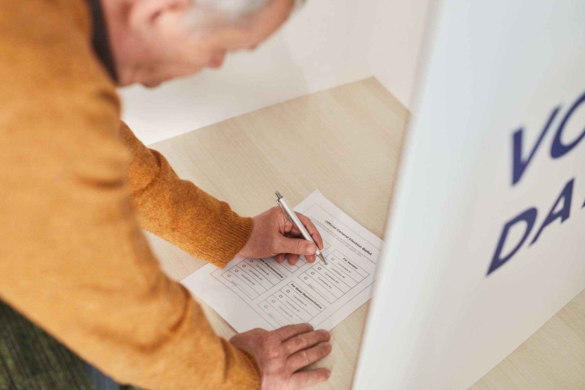 satire-image-76 Election Nebraska satire image: Senior man marking a ballot at a voting booth in an indoor polling station.