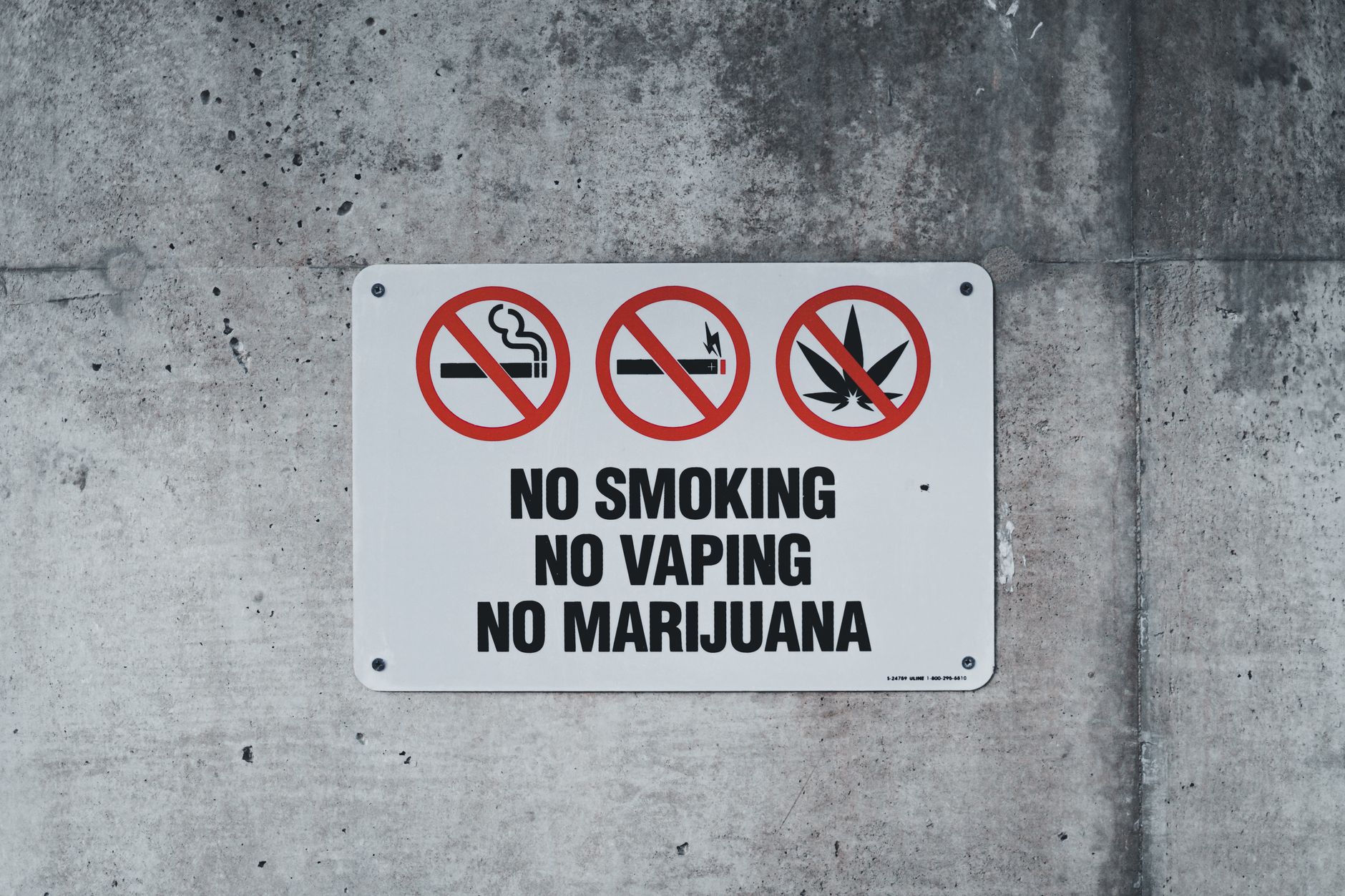 satire-image-83 Supreme Court Orders satire image: A clear warning sign prohibiting smoking, vaping, and marijuana on a concrete wall.